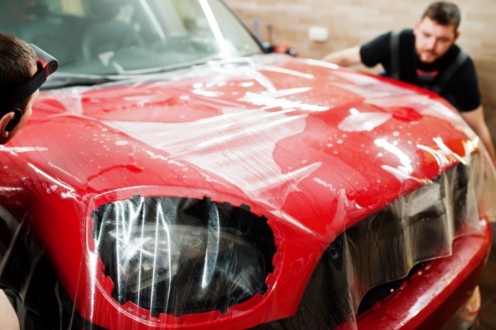 Professional installing Helmet PPF on a red car