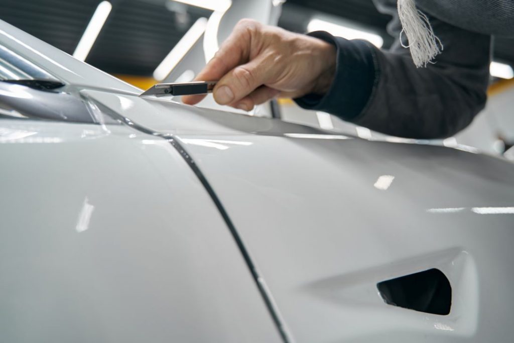 Close up picture of an installer trimming the Helmet PPF on a white car